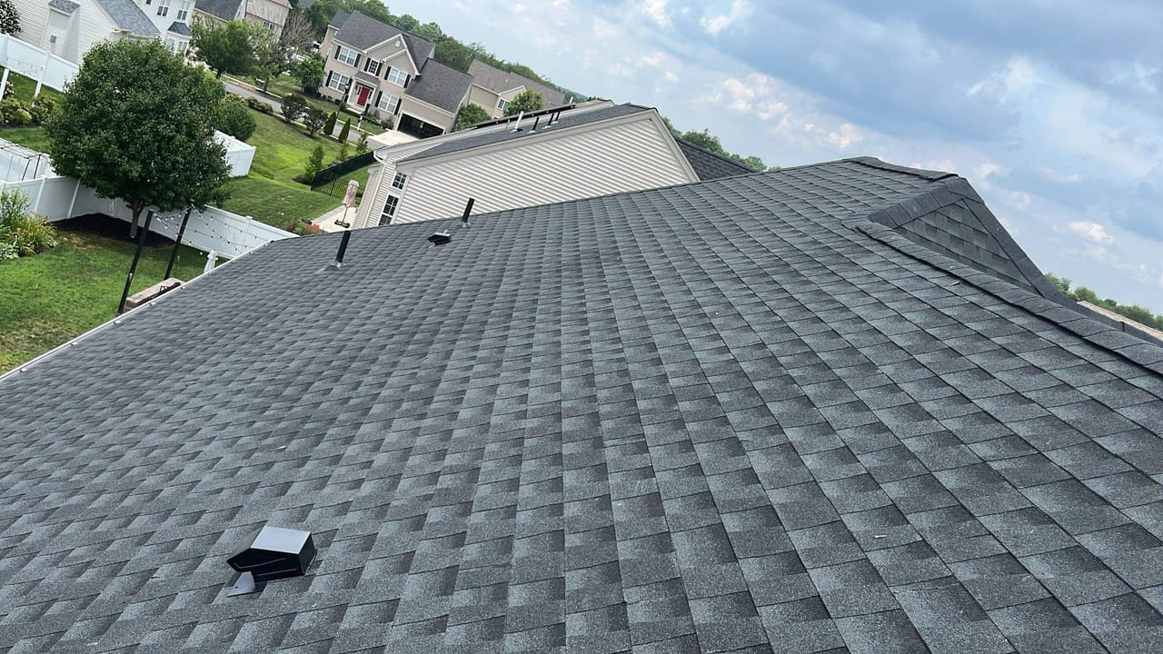New gray architectural shingle roof on a colonial home, with the neighborhood behind it