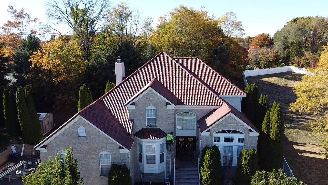 Aerial view of a two-story home with a new red Spanish tile roof, surrounded by autumn trees