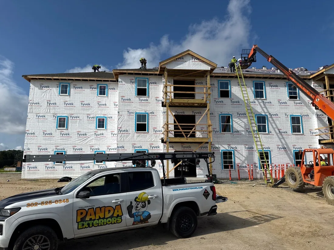 A Panda Exteriors crew roofing a new four-story building, with a Panda truck parked in front