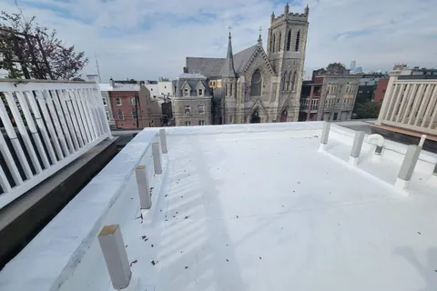 A new white flat roof on a city building, with church spires beyond